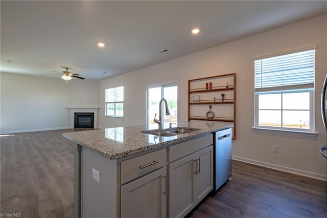 kitchen with a sink, dishwashing machine, ceiling fan, an island with sink, and dark wood-type flooring