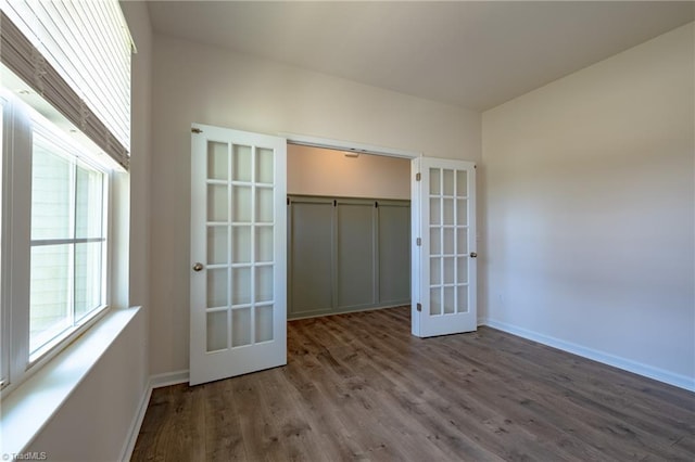 unfurnished bedroom with french doors, multiple windows, wood finished floors, and baseboards