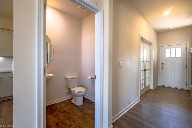 half bath with wood finished floors, toilet, baseboards, and backsplash