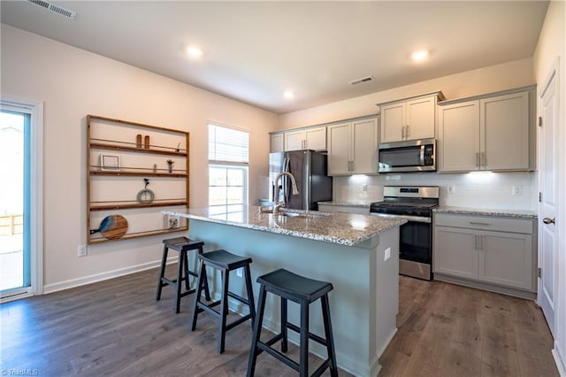 kitchen with appliances with stainless steel finishes, a kitchen breakfast bar, an island with sink, backsplash, and gray cabinets