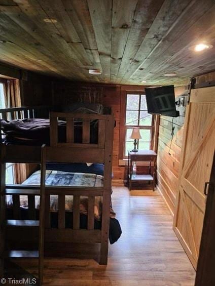 bedroom featuring a barn door, hardwood / wood-style floors, wooden ceiling, and wooden walls