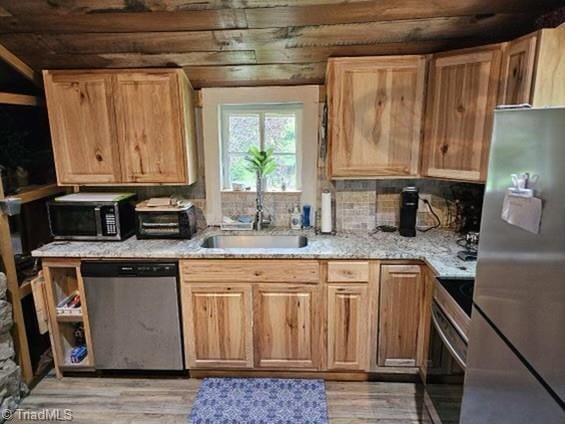 kitchen with light stone counters, sink, stainless steel appliances, and light wood-type flooring