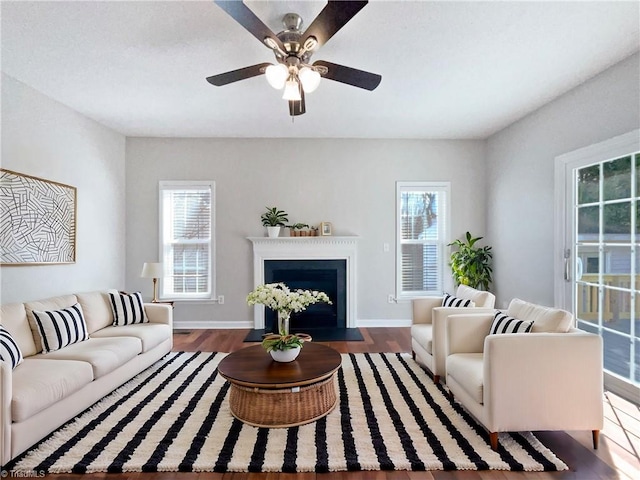 living room featuring a ceiling fan, a fireplace with flush hearth, wood finished floors, and baseboards