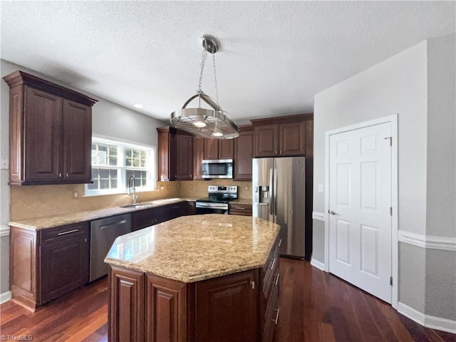 kitchen featuring dark wood-type flooring, light stone counters, a sink, a center island, and appliances with stainless steel finishes