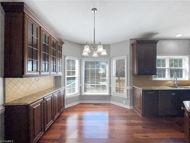 kitchen featuring a sink, glass insert cabinets, dark brown cabinetry, decorative backsplash, and dark wood-style flooring