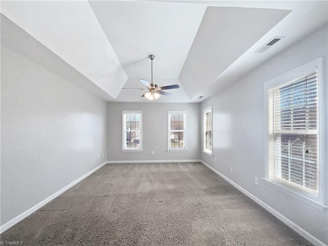 carpeted empty room with visible vents, a tray ceiling, baseboards, ceiling fan, and vaulted ceiling