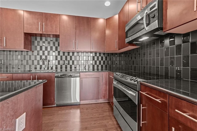 201 N Elm St Unit 703, Greensboro, NC 27401 - kitchen featuring stainless steel appliances, a sink, wood finished floors, dark countertops, and decorative backsplash