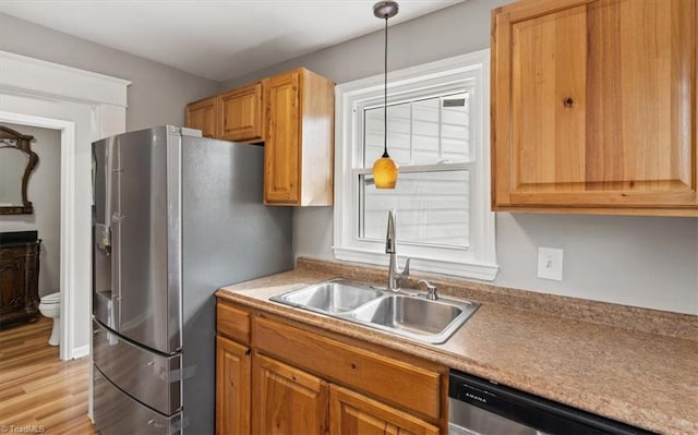 kitchen with light wood-type flooring, appliances with stainless steel finishes, sink, and decorative light fixtures