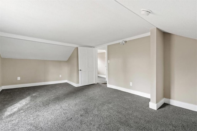additional living space featuring vaulted ceiling and dark colored carpet