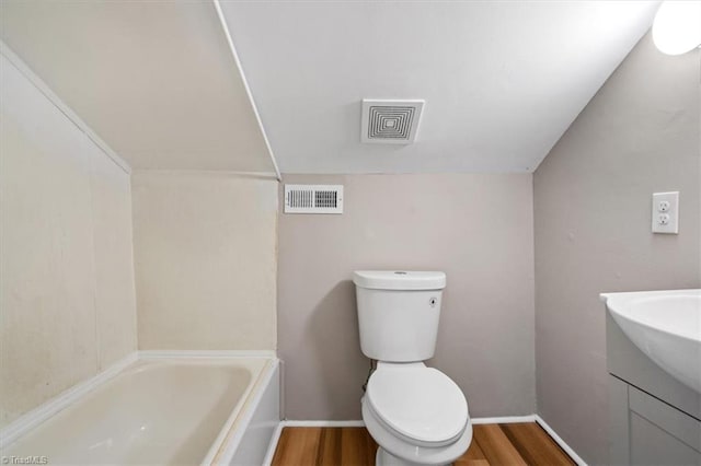 bathroom featuring toilet, vaulted ceiling, hardwood / wood-style floors, a washtub, and vanity