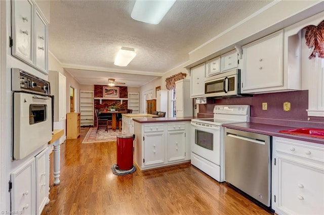 kitchen with light wood-type flooring, kitchen peninsula, stainless steel appliances, a textured ceiling, and white cabinets