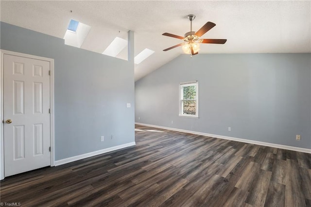 spare room featuring a ceiling fan, a textured ceiling, dark wood-style floors, vaulted ceiling with skylight, and baseboards