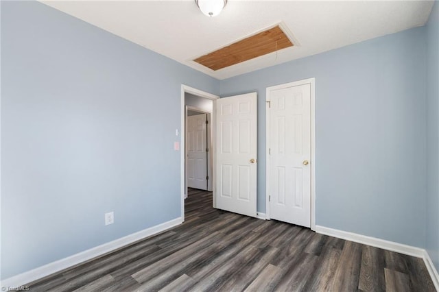 unfurnished bedroom with dark wood finished floors, attic access, and baseboards