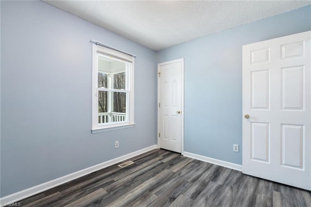 unfurnished bedroom with dark wood finished floors, visible vents, baseboards, and a textured ceiling