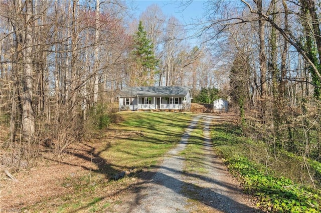 view of front facade featuring driveway, a shed, covered porch, an outdoor structure, and a front yard