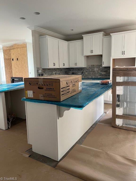 kitchen featuring tasteful backsplash, dark countertops, ornamental molding, and white cabinets