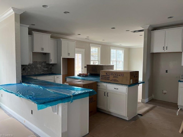 kitchen with backsplash, a kitchen island, crown molding, a peninsula, and white cabinets