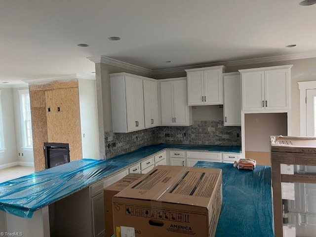 kitchen with white cabinets, a glass covered fireplace, crown molding, tasteful backsplash, and a center island