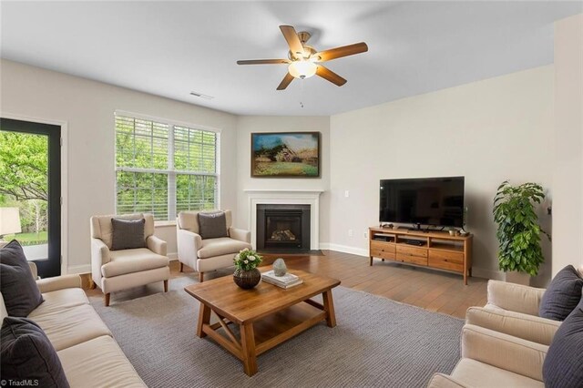 living room featuring plenty of natural light, baseboards, a ceiling fan, and a fireplace with flush hearth