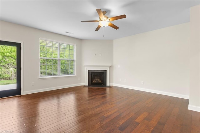 unfurnished living room with plenty of natural light, dark wood-style flooring, baseboards, and a ceiling fan