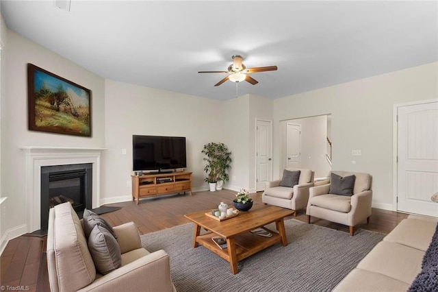living room featuring dark wood-type flooring, baseboards, ceiling fan, and a glass covered fireplace