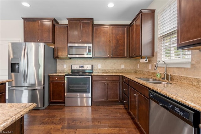 kitchen with a sink, dark wood finished floors, recessed lighting, light stone countertops, and appliances with stainless steel finishes