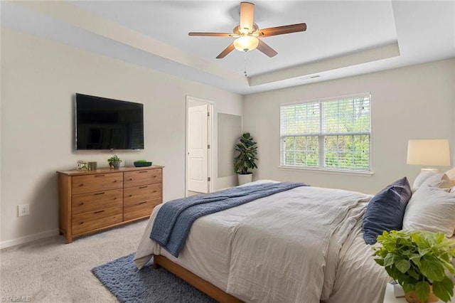 bedroom with light colored carpet, visible vents, ceiling fan, a raised ceiling, and baseboards