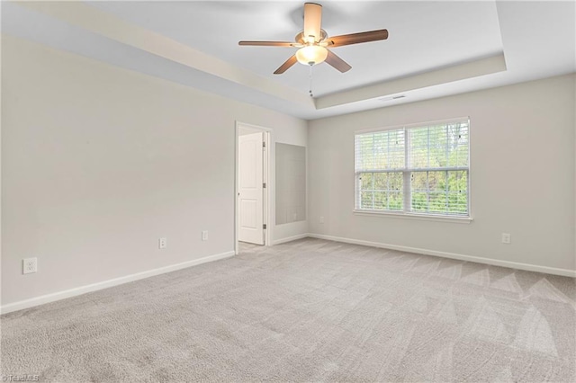 carpeted empty room with a tray ceiling, baseboards, and a ceiling fan