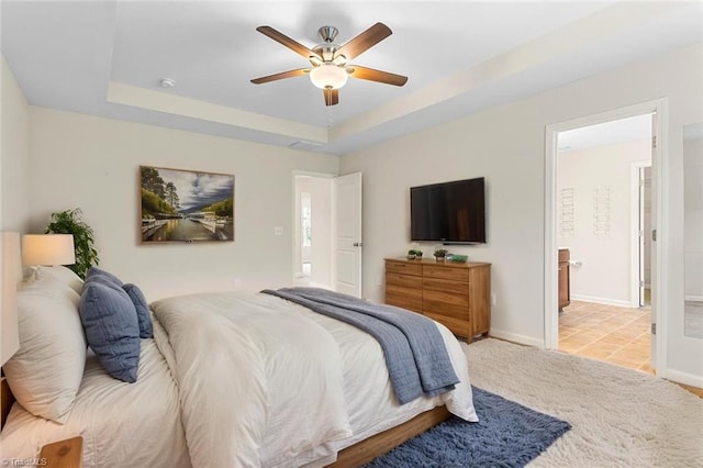 carpeted bedroom featuring a tray ceiling, baseboards, and ceiling fan