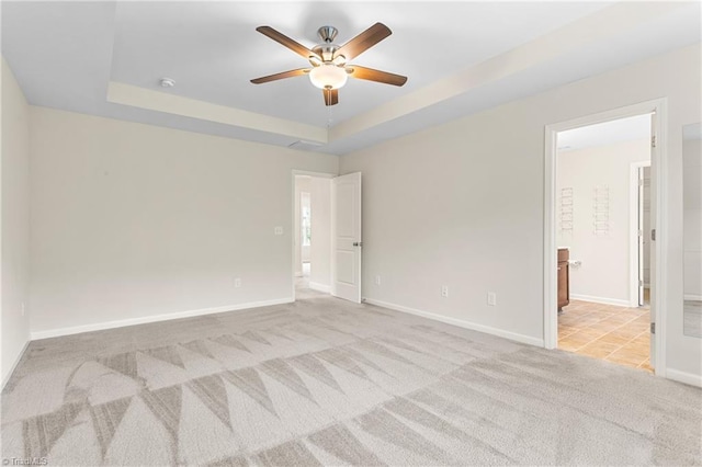 spare room featuring a ceiling fan, a raised ceiling, carpet flooring, and baseboards