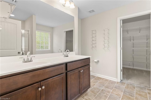 full bathroom with a sink, a stall shower, a spacious closet, double vanity, and baseboards