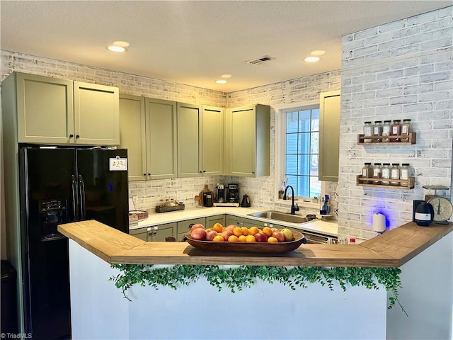 kitchen featuring brick wall, wooden counters, sink, black fridge, and kitchen peninsula