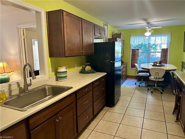 kitchen featuring ceiling fan, black fridge, sink, light tile patterned floors, and dark brown cabinets