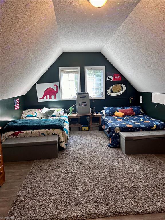 bedroom with vaulted ceiling, a textured ceiling, and hardwood / wood-style flooring