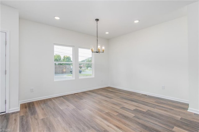 empty room featuring recessed lighting, wood finished floors, baseboards, and an inviting chandelier