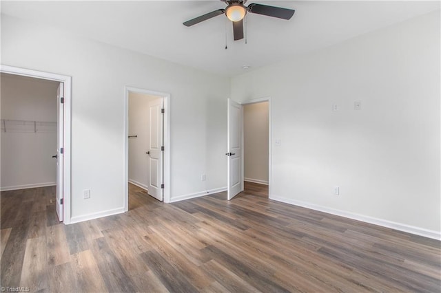 unfurnished bedroom featuring a closet, a spacious closet, dark wood-type flooring, a ceiling fan, and baseboards