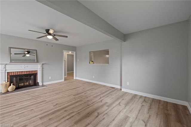 unfurnished living room featuring a brick fireplace, light hardwood / wood-style floors, beamed ceiling, and ceiling fan