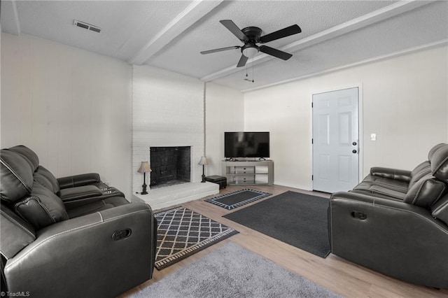 living room with a fireplace, a textured ceiling, ceiling fan, hardwood / wood-style flooring, and beamed ceiling