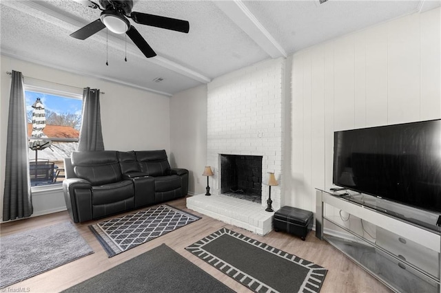 living room with beamed ceiling, light hardwood / wood-style floors, a textured ceiling, and a brick fireplace