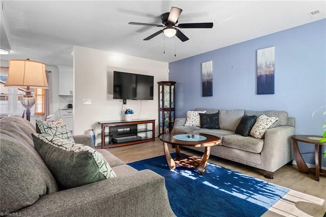 living room with ceiling fan, light hardwood / wood-style flooring, and a textured ceiling