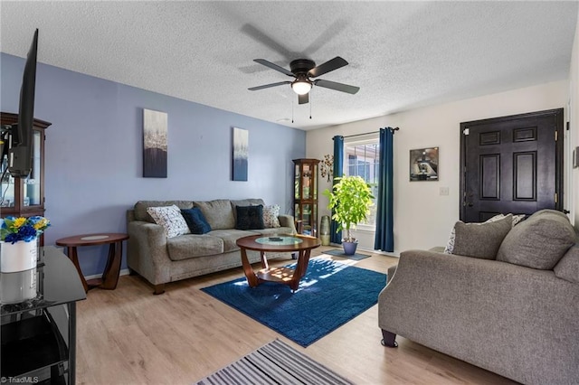 living room featuring ceiling fan, light hardwood / wood-style flooring, and a textured ceiling