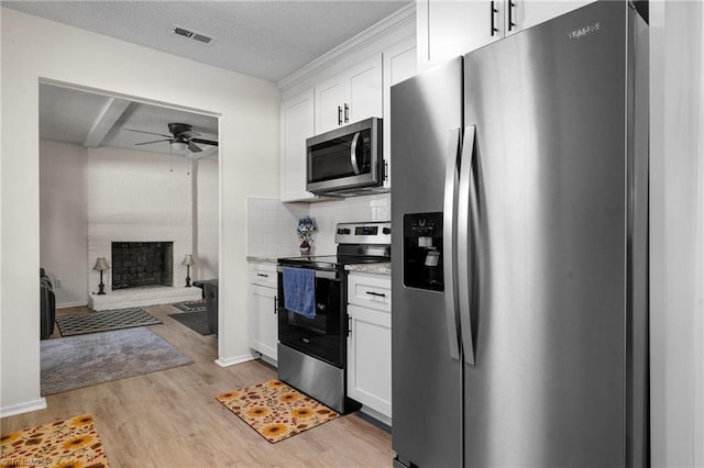 kitchen featuring white cabinetry, a large fireplace, ceiling fan, stainless steel appliances, and light wood-type flooring