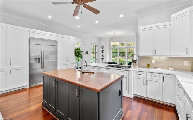 kitchen featuring a center island with sink, light stone counters, white cabinets, sink, and appliances with stainless steel finishes