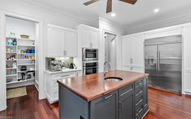 kitchen with gray cabinetry, a center island with sink, built in fridge, sink, and white cabinets