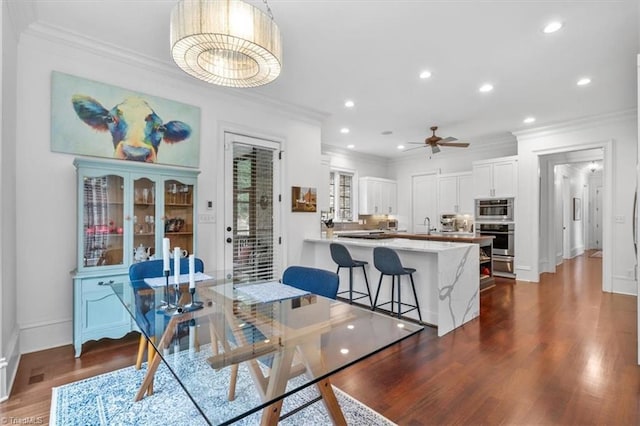 dining space with dark wood-type flooring, ceiling fan, sink, and crown molding