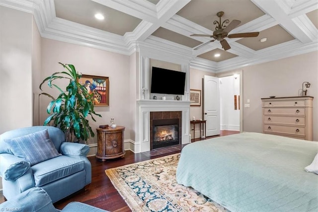 bedroom featuring crown molding, coffered ceiling, dark wood-type flooring, a tile fireplace, and ceiling fan