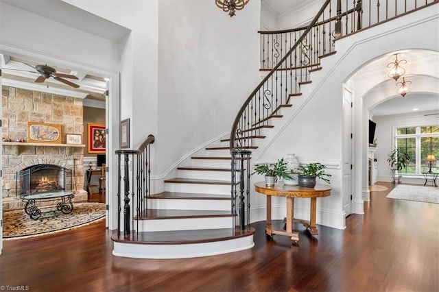 stairway featuring ornamental molding, hardwood / wood-style floors, a high ceiling, and a stone fireplace