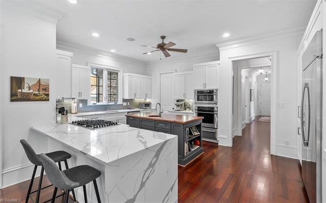 kitchen with appliances with stainless steel finishes, kitchen peninsula, light stone counters, a kitchen island, and white cabinets