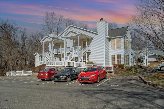 view of front of house with uncovered parking, a porch, and a chimney