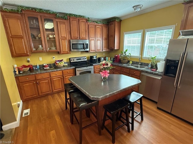 kitchen with appliances with stainless steel finishes, a sink, brown cabinetry, light wood-style flooring, and a textured ceiling